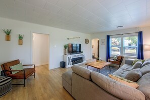 A modern living room with a sofa, a coffee table, and a TV. There are two wooden cabinets and a door leading to another room.