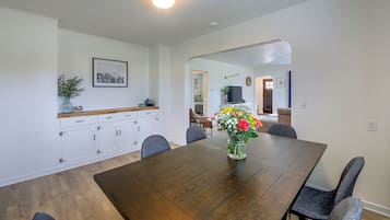 A dining area with a wooden table, chairs, a vase with flowers, and a kitchen area with cabinets and a countertop.