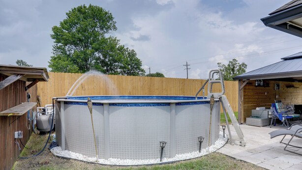 A rectangular above-ground pool with a ladder, surrounded by a wooden fence, and equipped with a water pump and hoses. - Home w/ Pool & Outdoor Entertainment in Gonzales (Gonzales)