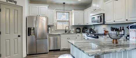 A modern kitchen with white cabinetry, stainless steel appliances, a marble countertop, and a hanging light fixture.