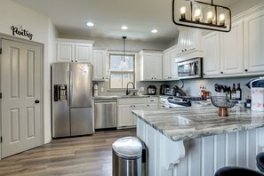 Una cocina moderna con armarios blancos, electrodomésticos de acero inoxidable, encimera de mármol e iluminación colgante.