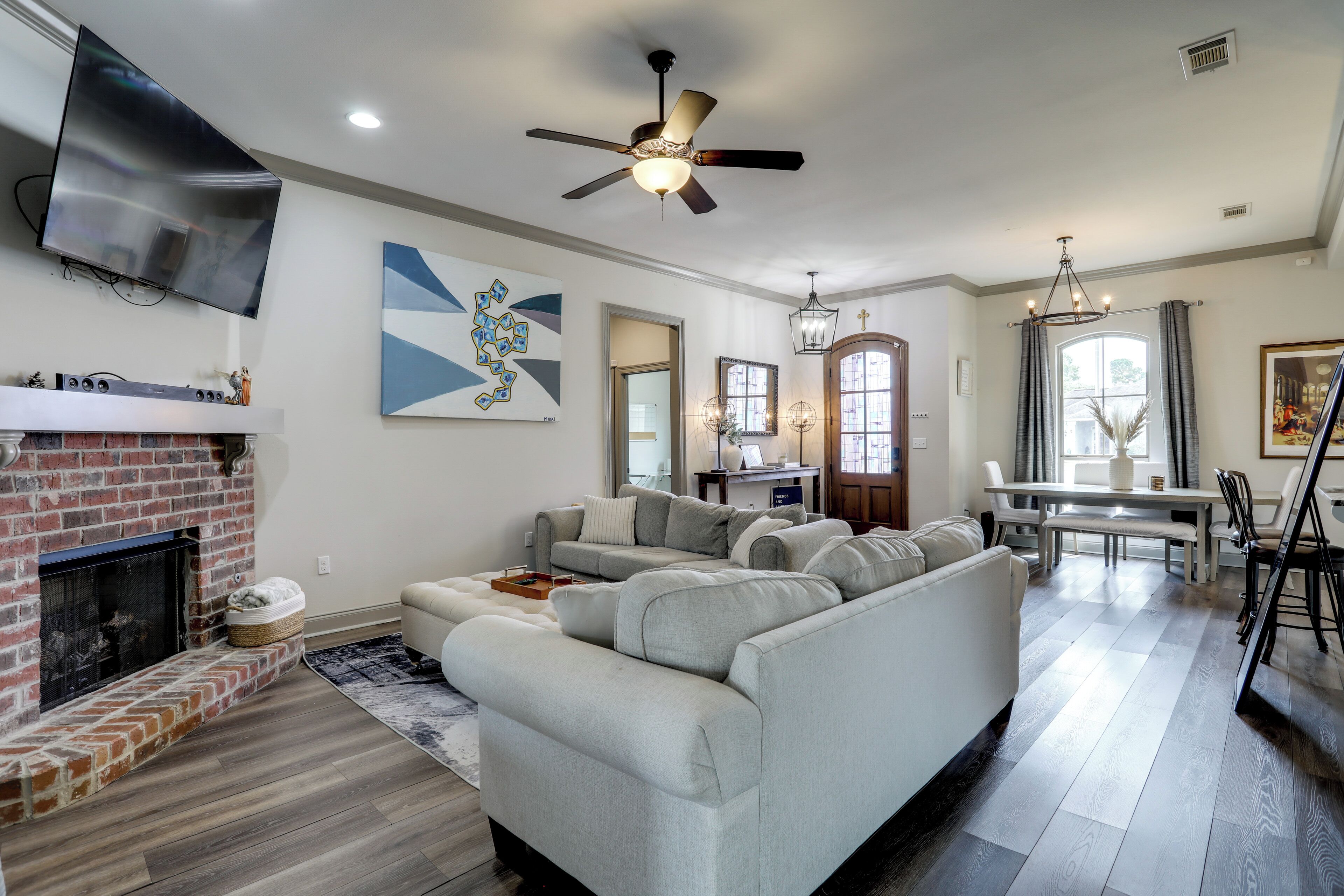 A living room with a fireplace, a grey sectional sofa, a ceiling fan, and a dining area with a table and chairs.