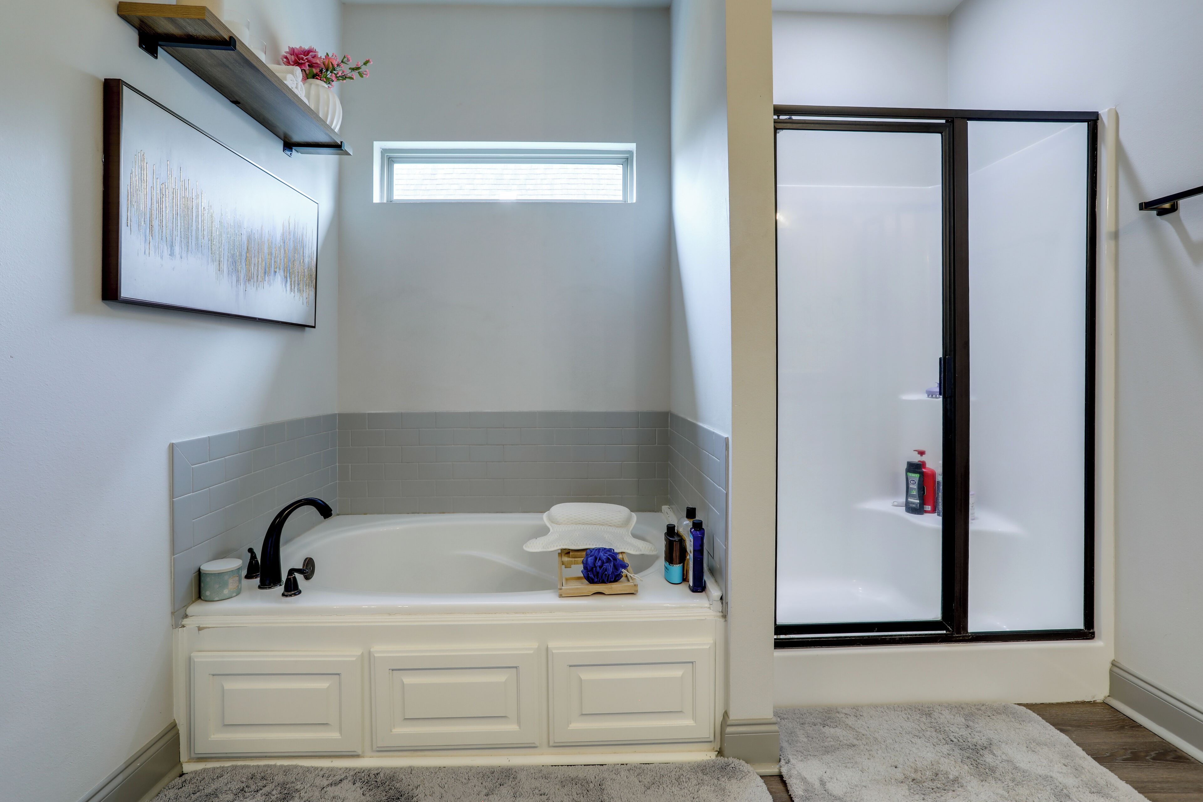 A bathroom with a white bathtub, a shower enclosure, and a framed artwork on the wall.