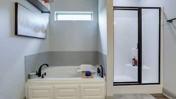 A bathroom with a white bathtub, a shower enclosure, and a framed artwork on the wall.