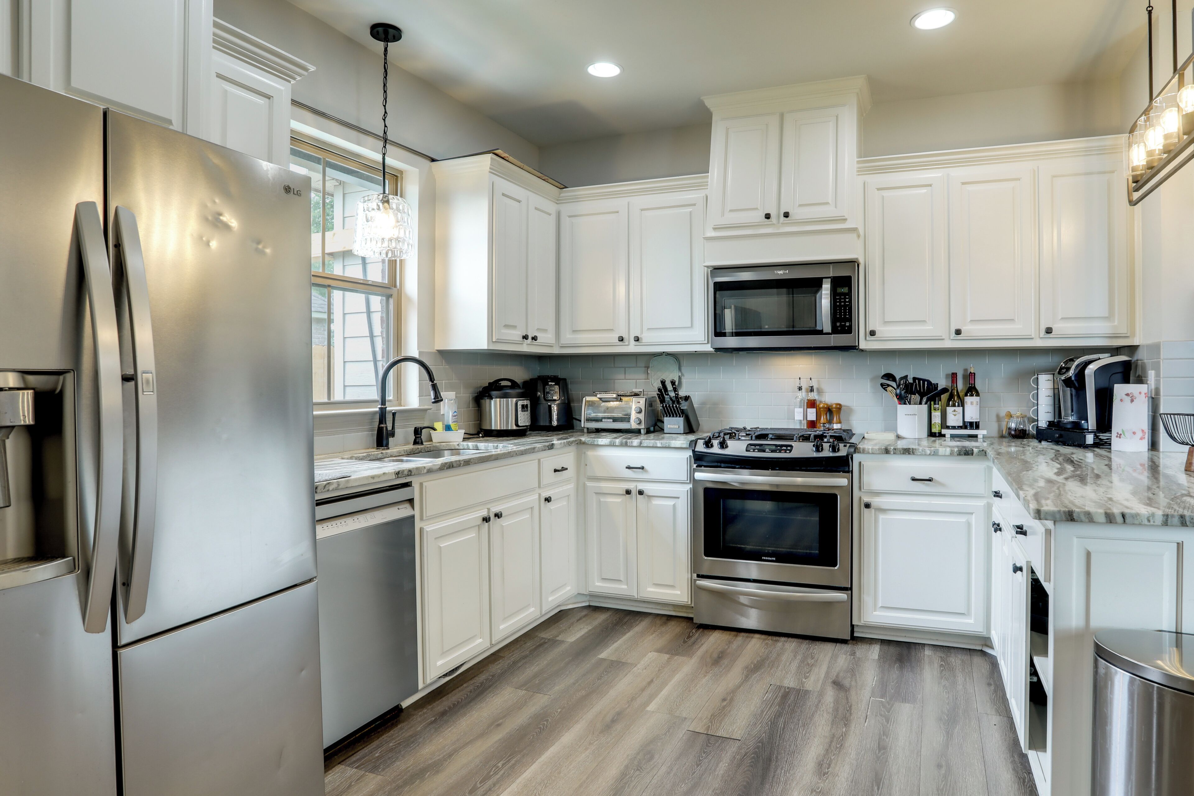 A modern kitchen with white cabinets, stainless steel appliances, and a wooden floor.