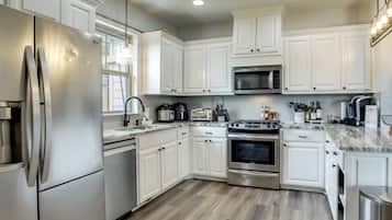 A modern kitchen with white cabinets, stainless steel appliances, and a wooden floor.