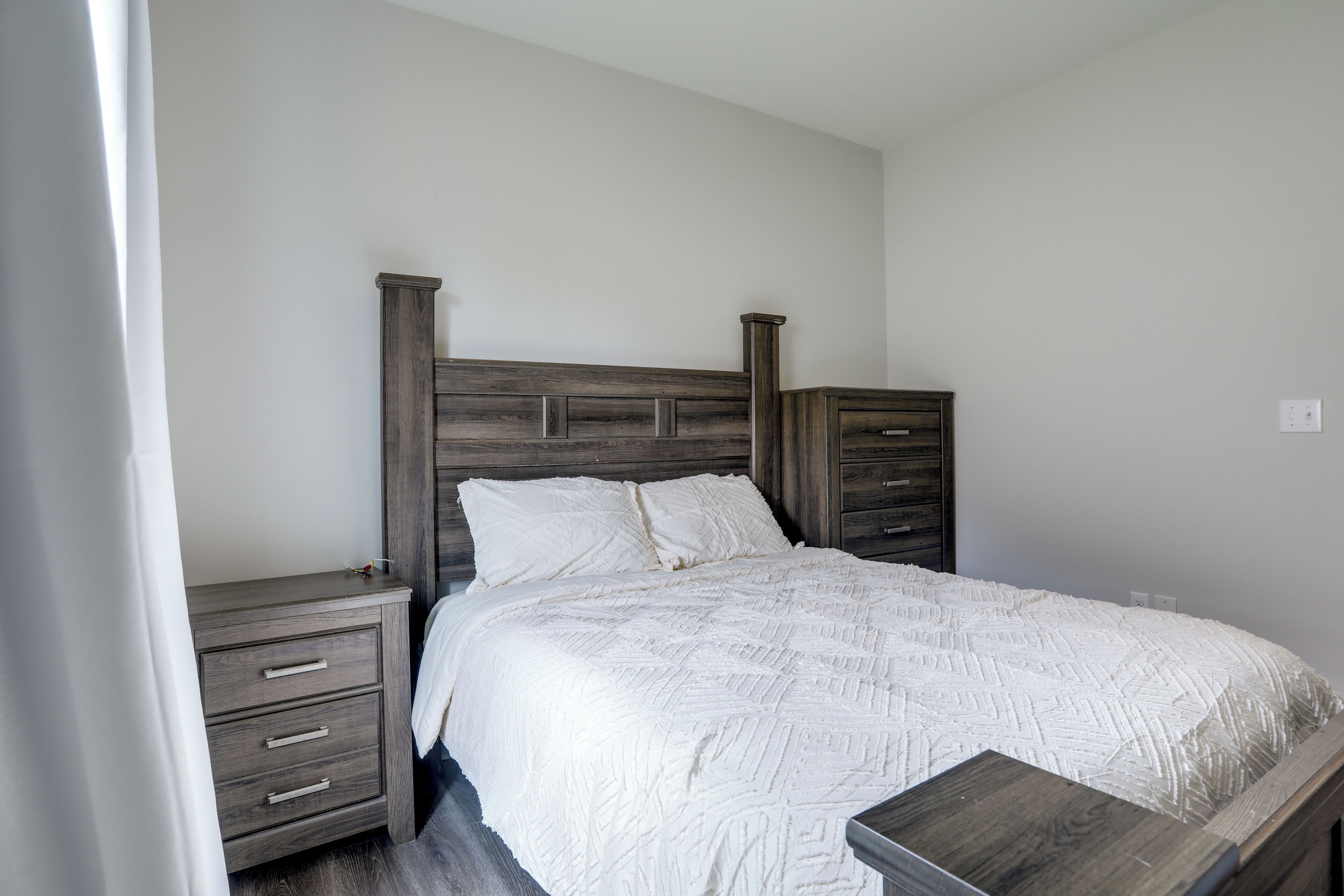 Une chambre à coucher avec une tête de lit en bois, un couvre-lit blanc et une table de chevet dotée de tiroirs.