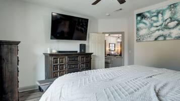 A bedroom with a large bed, a television mounted on the wall, a ceiling fan, and a painting on the wall.