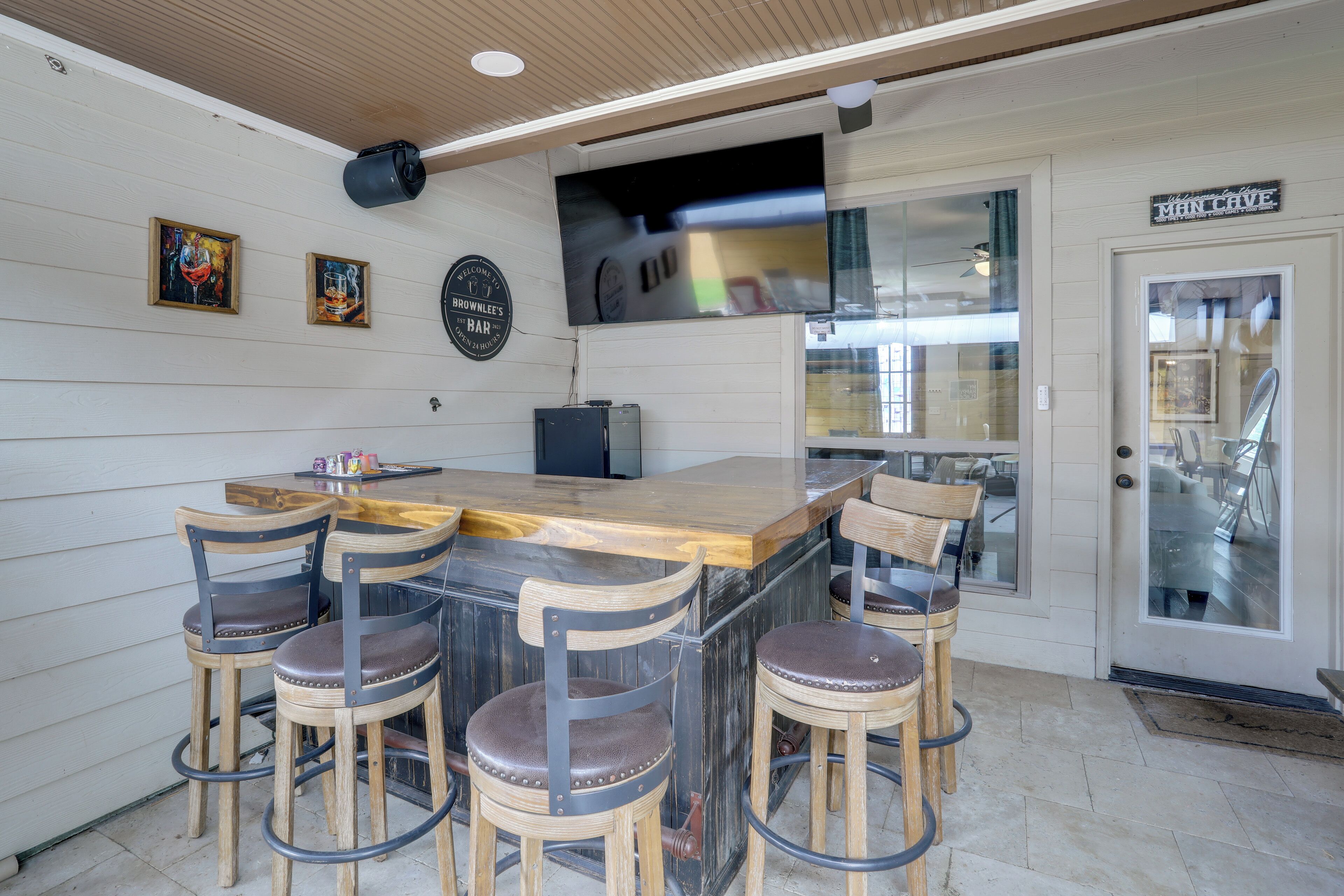 A bar area with wooden stools, a bar counter, and a television mounted on the wall.