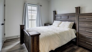 A bedroom with a wooden bed, a nightstand, a dresser, and a window with curtains. - Home w/ Pool & Outdoor Entertainment in Gonzales (Gonzales)