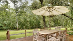 An outdoor wooden deck with a table and chairs, surrounded by a wooden railing, set against a backdrop of dense trees and greenery. - 2 Mi to Silver Springs State Pk! Family Hideaway (Silver Springs)