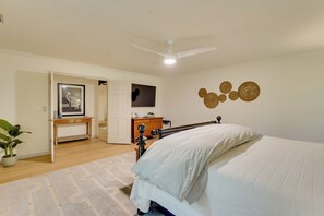 Ein Schlafzimmer mit einem Bett, einem Deckenventilator, einer Kommode, einem Schreibtisch und einem an der Wand montierten Fernseher.