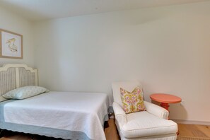 Un dormitorio con cama, una silla, una mesita redonda y un cuadro colgado en la pared.