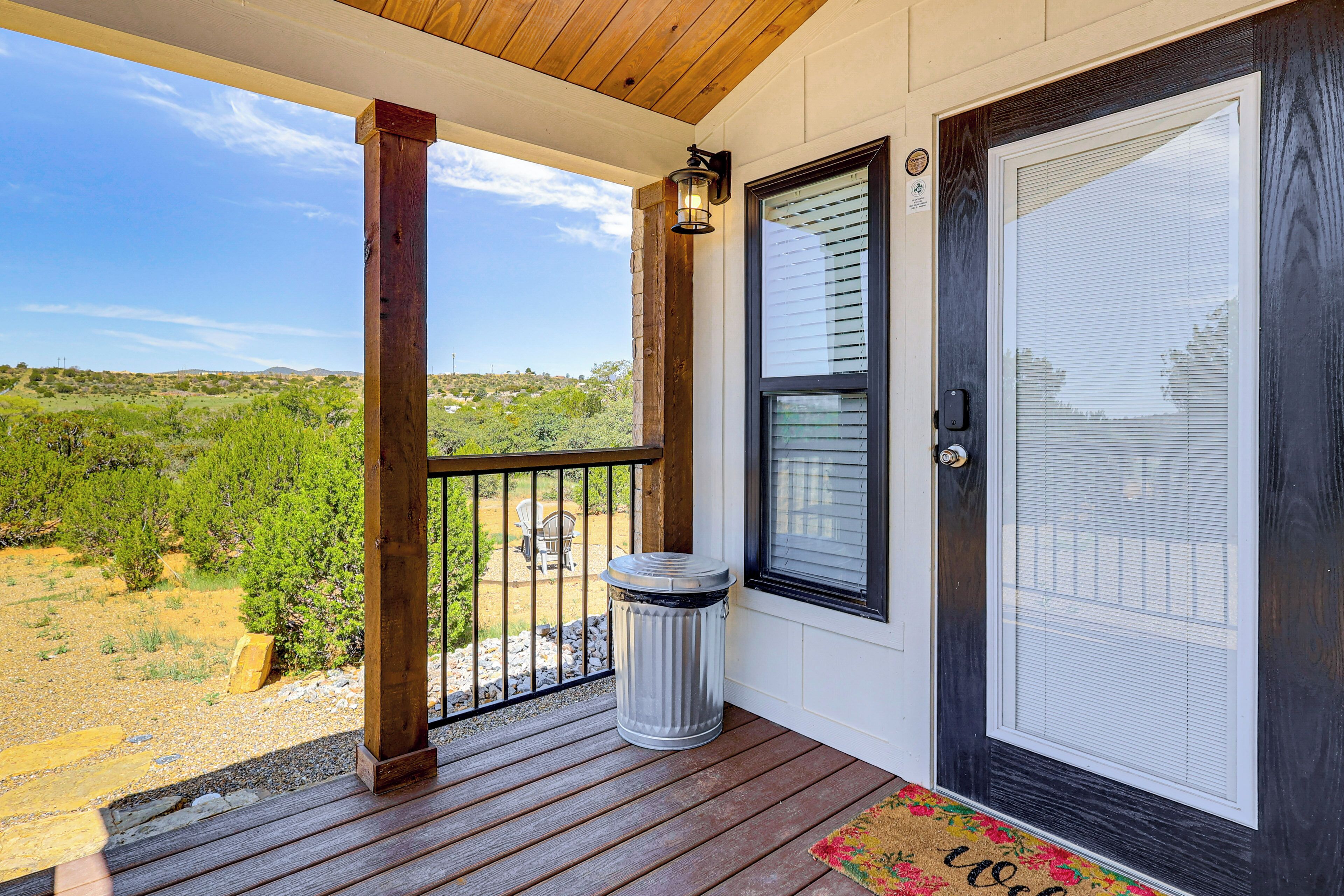 A porch with a view of a green landscape, a trash can, and a door with a window.