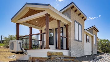 Una casa moderna con porche cubierto, fachada de piedra y unidad de aire acondicionado.