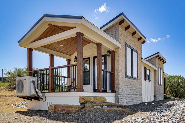 A modern house with a covered porch, stone exterior, and an air conditioning unit.