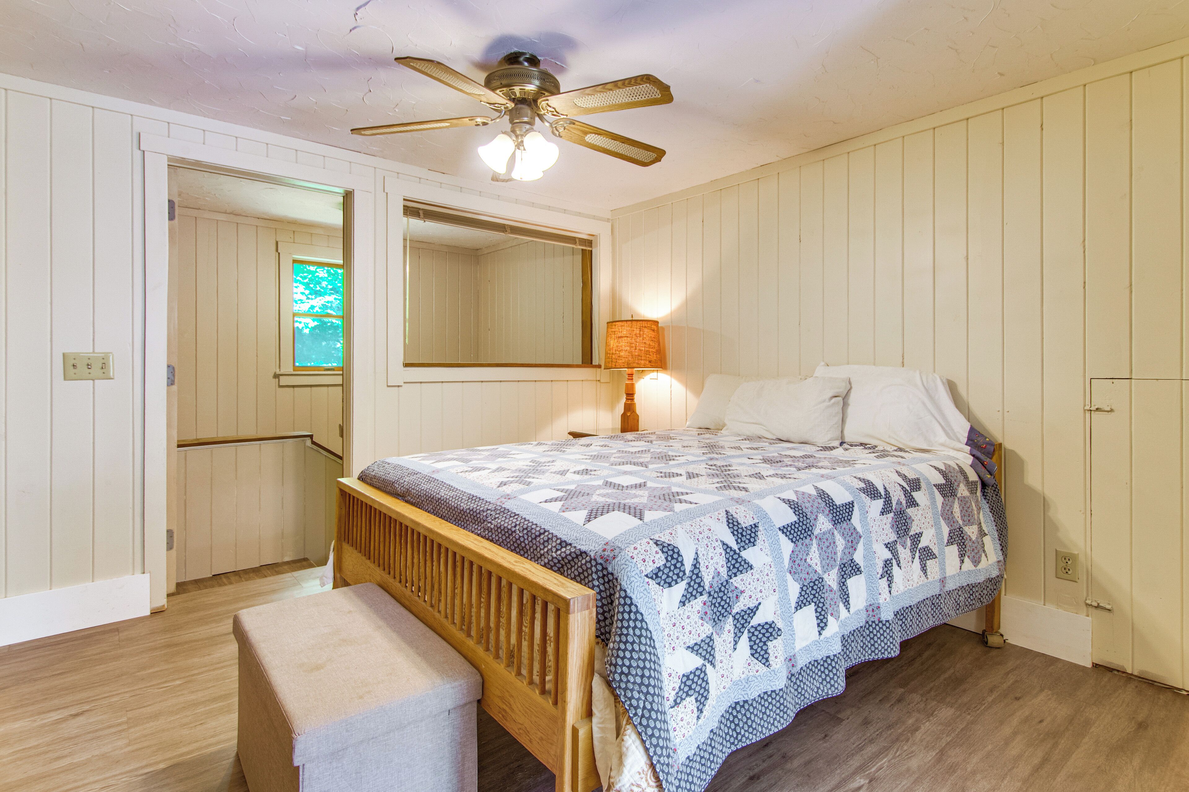 Un dormitorio con cama de madera, un banco, un ventilador de techo y una ventana.
