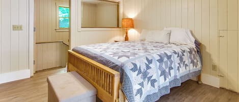 Un dormitorio con cama de madera, un banco, un ventilador de techo y una ventana.