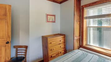 A room with a wooden dresser, a chair, a bed with a striped bedspread, a framed picture on the wall, and a window with blinds.
