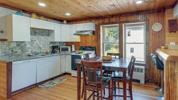 A kitchen with white cabinets, a granite countertop, a stove, and a dining area with wooden chairs and a table.