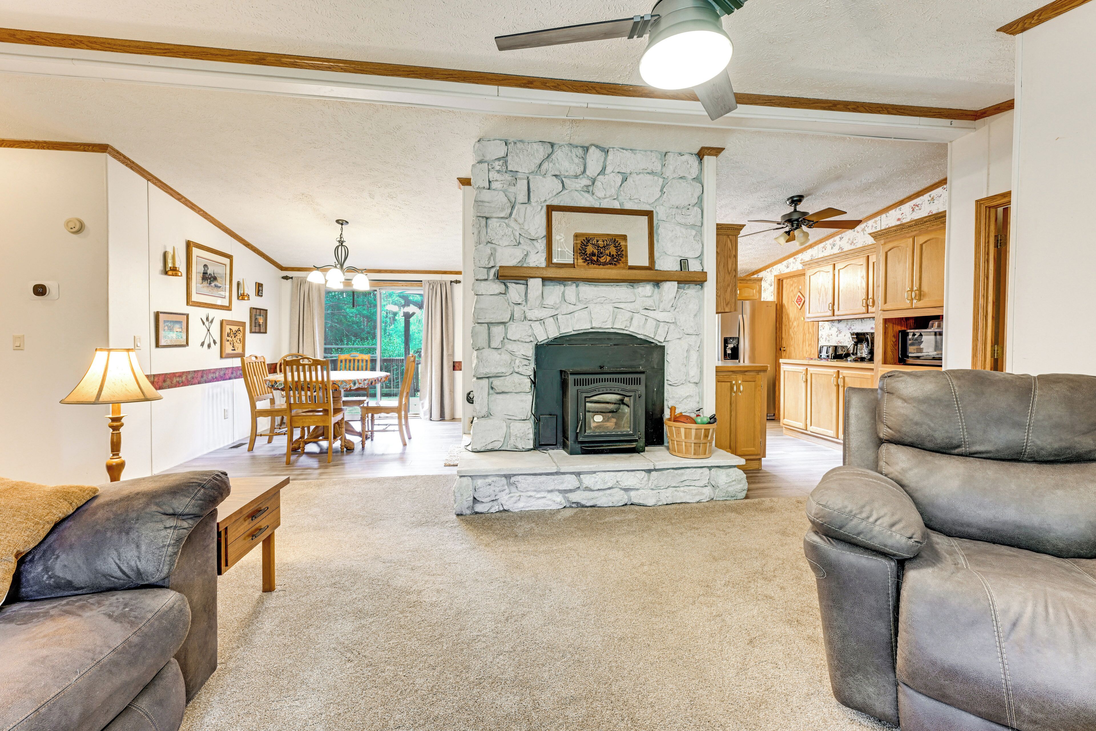 A living room with a stone fireplace, a dining area with chairs, and a kitchen with wooden cabinets.