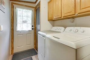 Une buanderie équipée d’un lave-linge et d’un sèche-linge à chargement frontal, de placards en bois au-dessus, et d’une porte avec une fenêtre.