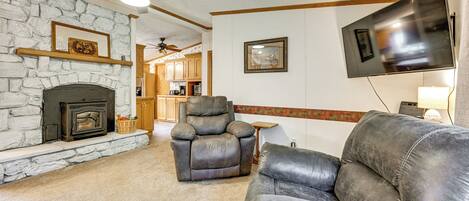 A living room with a stone fireplace, leather recliner, and a flat-screen TV mounted on the wall.