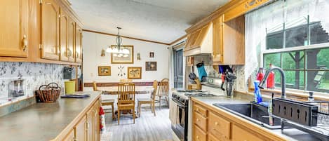 A kitchen with wooden cabinets, a dining table with chairs, a stove, and a large window.