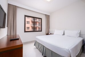 A hotel room with a bed, a TV, a desk, and a window with a view of buildings. - Beautiful Apart With Pool in Luxury Resort Jbv152 (Florianópolis)