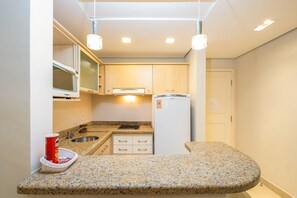 A compact kitchen with granite countertops, a microwave, a stove, and a refrigerator. - Beautiful Apart With Pool in Luxury Resort Jbv152 (Florianópolis)