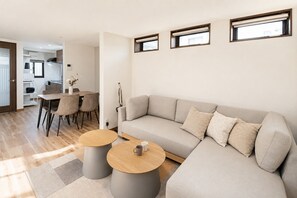 Ein modernes Wohnzimmer mit einer Couch, zwei runden Tischen, einer Essecke mit Stühlen und einer Küche im Hintergrund.