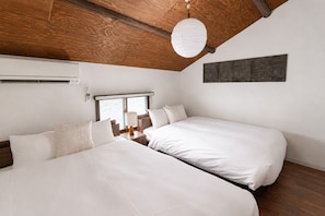 Ein Hotelzimmer mit zwei Betten, einer Holzbalkendecke, einem Fenster mit Aussicht und einem an der Wand hängenden Kunstwerk.