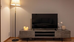 A modern living room with a flat-screen TV on a grey cabinet, a floor lamp, and candles on a small table. - AYA - Self Check-In Only (Osaka, Chuo Ward)