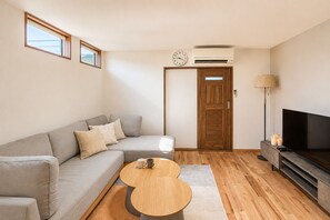 A modern living room with a grey sectional sofa, two round wooden coffee tables, a flat-screen TV, and a wooden door. - AYA - Self Check-In Only (Osaka, Chuo Ward)