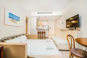 A hotel room with a bed, a sofa, a TV, a small kitchen area, and a painting on the wall. - Great ap With Pool in Resort in Jurere Jbv157 (Florianópolis)