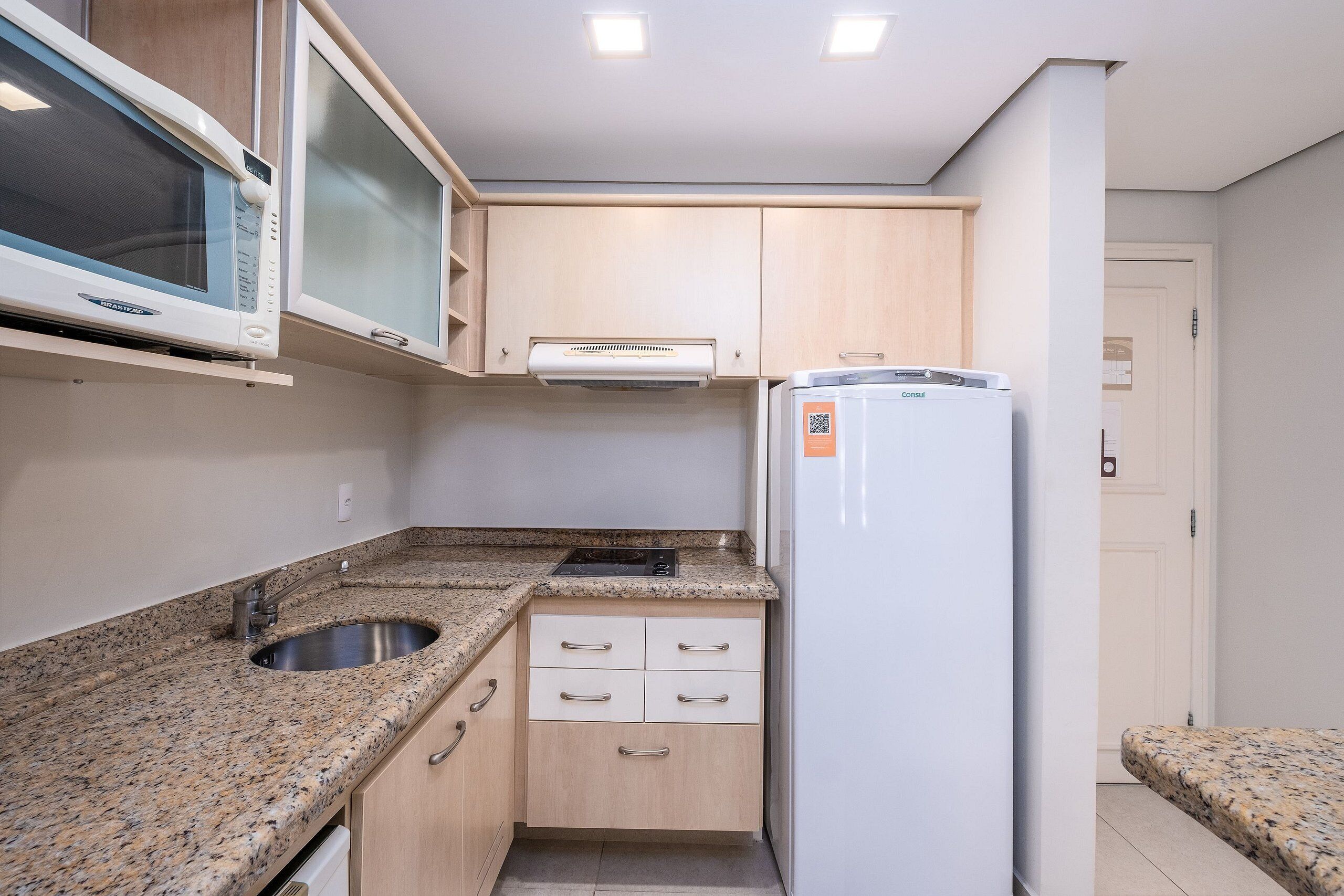 A compact kitchen with a microwave, stove, sink, and a refrigerator.
