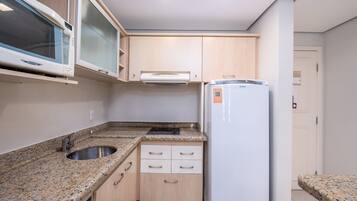 A compact kitchen with a microwave, stove, sink, and a refrigerator.