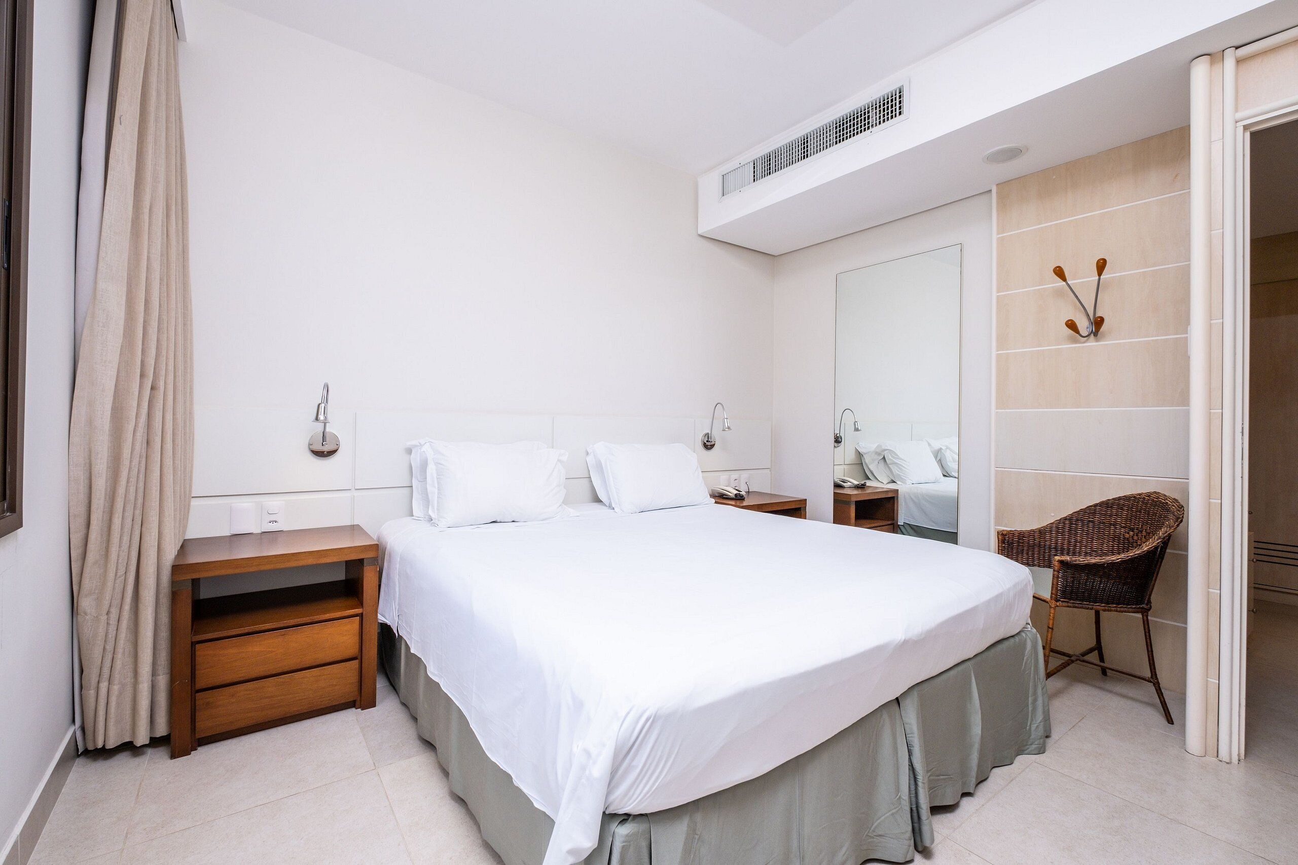 A hotel room with a large bed, bedside tables, a chair, a mirror, and a wardrobe.
