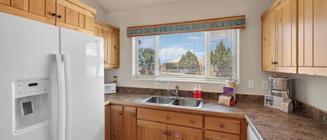A kitchen with wooden cabinets, a white refrigerator, a sink, and a window with blinds.