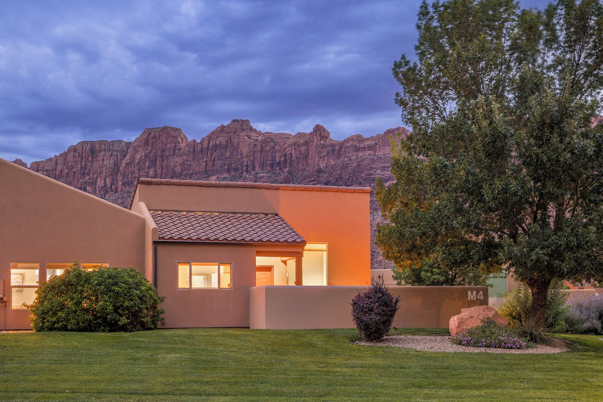 A modern house with a flat roof, a well-maintained lawn, and a mountain backdrop.