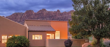 A modern house with a flat roof, a well-maintained lawn, and a mountain backdrop.
