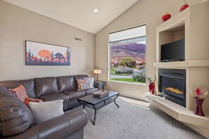 Una sala de estar con un sofá de cuero, una mesa de centro, una chimenea y un ventanal con vistas a un paisaje montañoso.