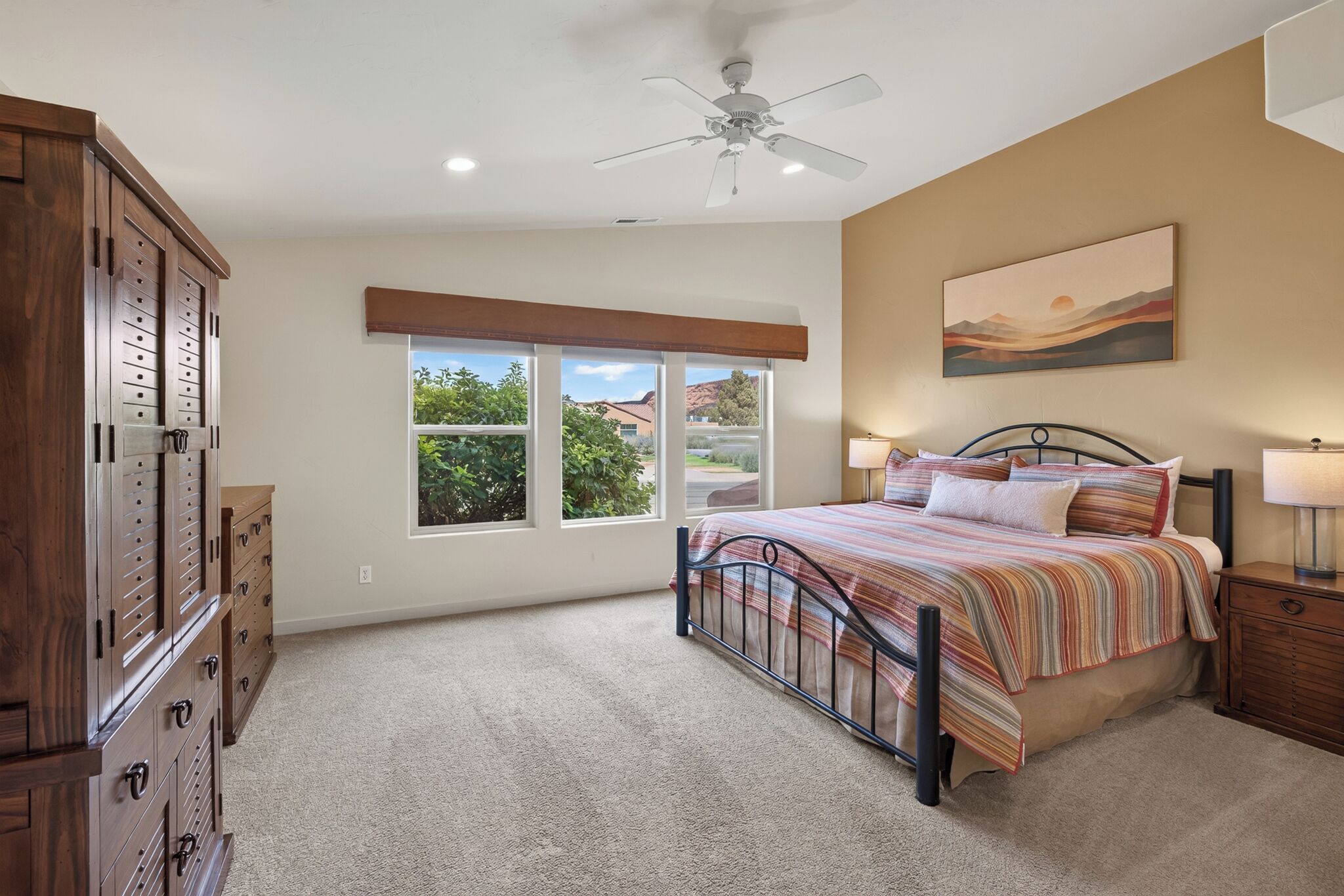 A bedroom with a bed, a ceiling fan, a window, and a painting on the wall.