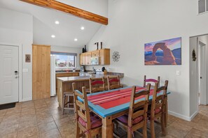 Une cuisine avec des meubles de rangement en bois, un îlot central et un coin repas avec des chaises en bois et une nappe colorée.
