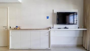 Quarto com televisão na parede, um armário branco e uma porta.