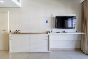 Quarto com televisão na parede, um armário branco e uma porta.