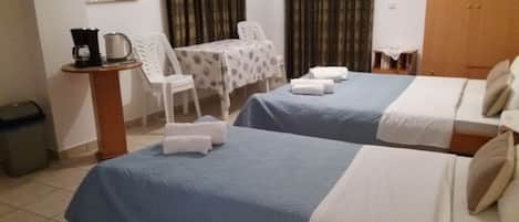 A hotel room with two beds, a small table with chairs, a coffee maker, and a trash bin.