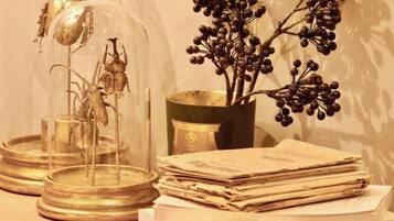 A table with a glass dome containing a metallic sculpture, a vase with dark berries, and a stack of papers.