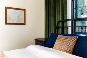 Una camera da letto con un letto, un comodino, un quadro incorniciato e tende verdi.