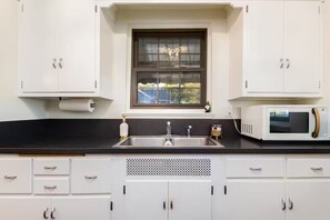 A kitchen with white cabinets, a black countertop, a sink, a window, and a microwave. - Clover Cottage - 1 mile to ND - Cozy Getaway (South Bend)